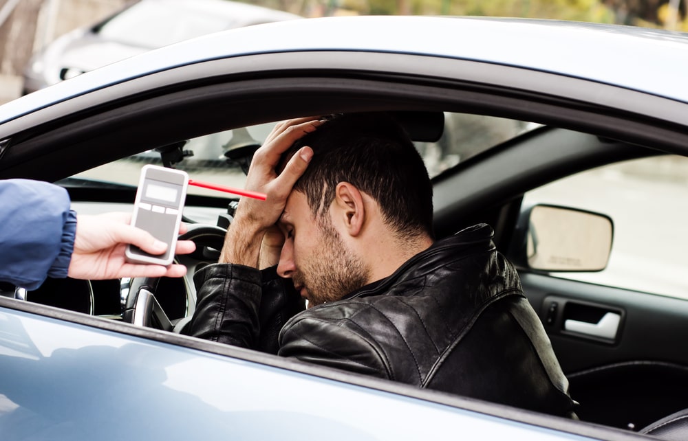 Driver Holding His Head And A Police Officer Handing Him A Breathalyser Test