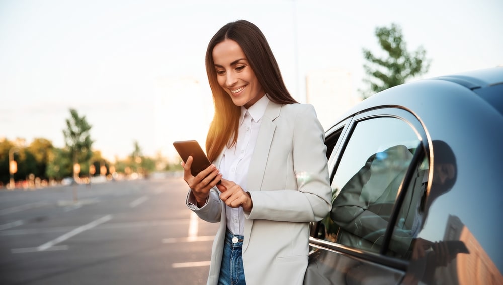 Woman Standing By Her Car And Looking At Her Phone