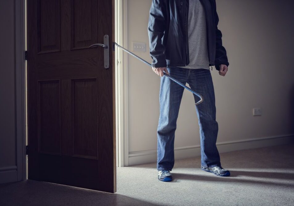 Intruder holding crowbar in dimly lit room.