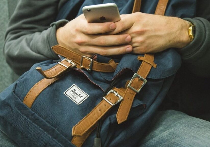 Person holding phone over blue backpack.