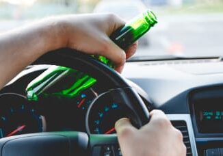 Driver holding beer bottle while steering car.