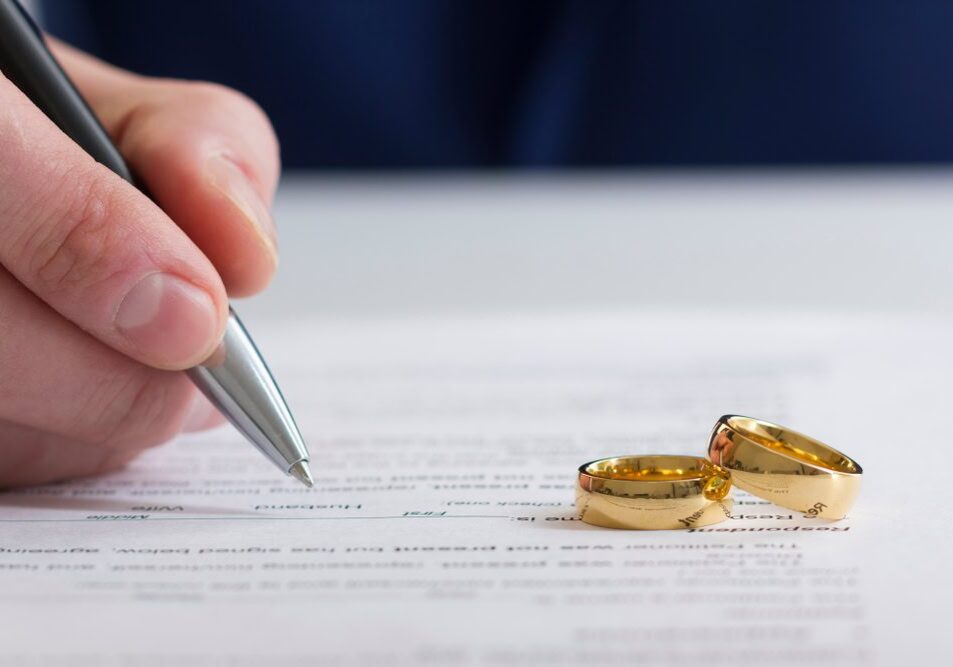 Signing document with gold wedding rings nearby.