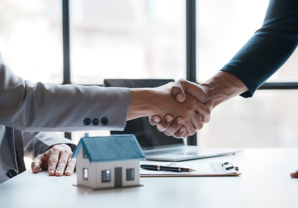 Handshake over miniature house on table.